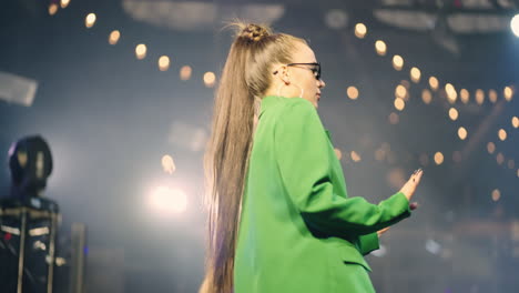 a young woman in a green jacket dances on stage in a nightclub.