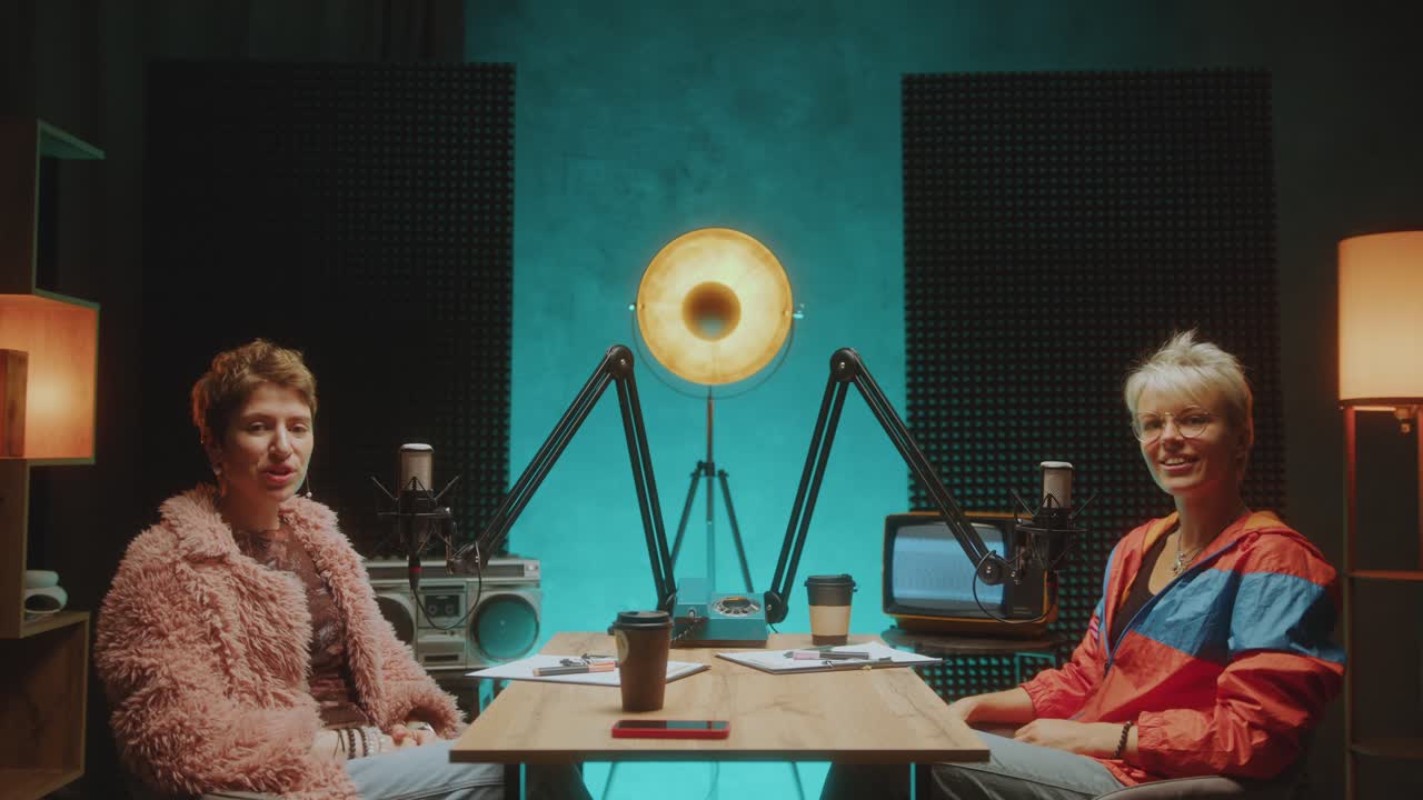 Two Young Female Bloggers Waving at Camera and Recording Podcast in Studio