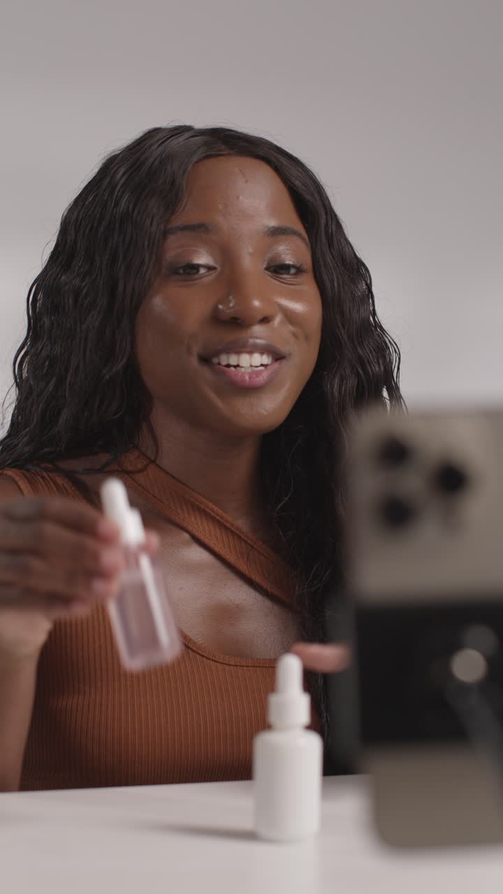 joven grabando belleza maquillaje revisión o tutorial para suero de cuidado de la piel en teléfono móvil para cargar en el canal de redes sociales 1