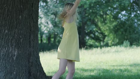 woman in yellow dress dancing by tree in summer park