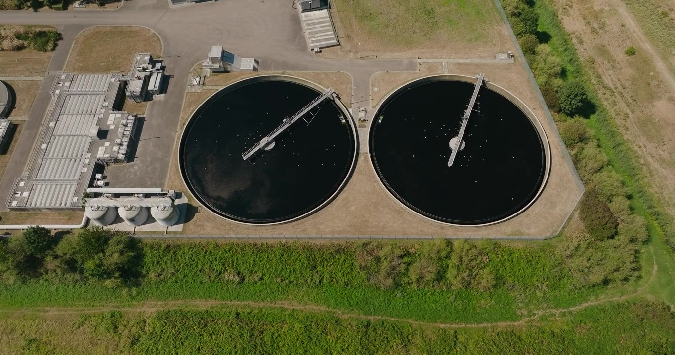 Top down drone pushes toward two large sedimentation basins at a wastewater treatment plant, highlighting water purification infrastructure and the wastewater settling process.
