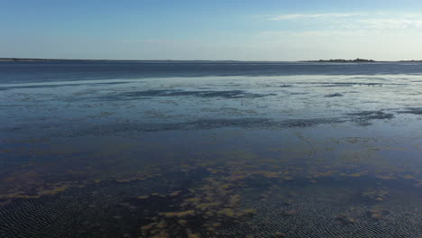 low aerial flight over shallow coral reef to coastal open water beyond