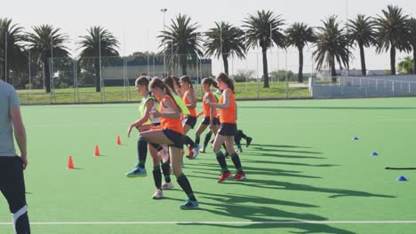 Coach-watching-female-hockey-players-exercising-on-the-field