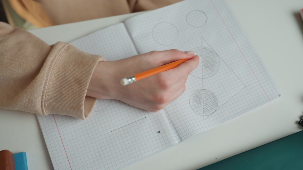 Primo piano di una mano che disegna cerchi su un quaderno. Un tutor a domicilio insegna grammatica attraverso schizzi a matita, con la manica di un morbido maglione appoggiata sulla scrivania. La carta a quadretti mostra diagrammi ombreggiati, in un'atmosfera di studio calma e concentrata.
