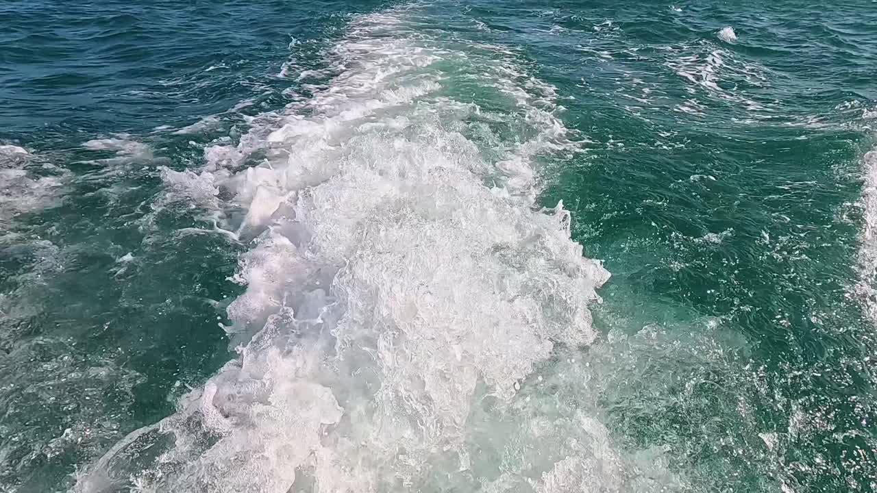 A boat creates a dynamic wake in clear turquoise waters, captured with steady camera movement under bright daylight
