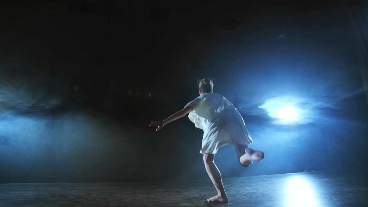 una escena dramática de ballet moderno una bailarina solitaria en un vestido blanco realiza pasos de baile usando coreografía moderna.