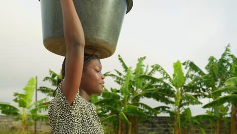 Fetching-water,-a-local-girl-carries-a-huge-basin-placed-on-top-of-her-head-in-one-of-the-villages-in-Kumasi,-Ghana,-Africa