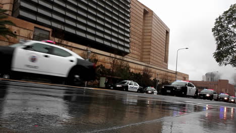 a line of police vehicles pass along a street on a rainy day