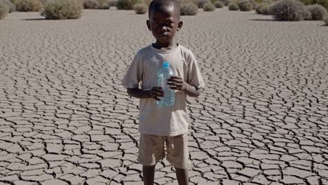 vulnerable african child standing amid barren lake bed, gripping water bottle with hope, symbolizing survival struggle against harsh environmental conditions and resource scarcity in arid regions