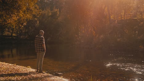 young man gazes at sparkling river in forest, feeling calm and introspective. sunlight and trees create soothing ambiance.