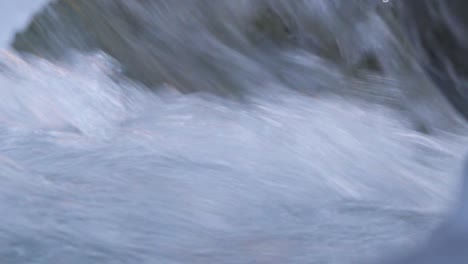 arroyo de montaña nevado, primer plano de agua fría que fluye rápidamente y brilla entre rocas