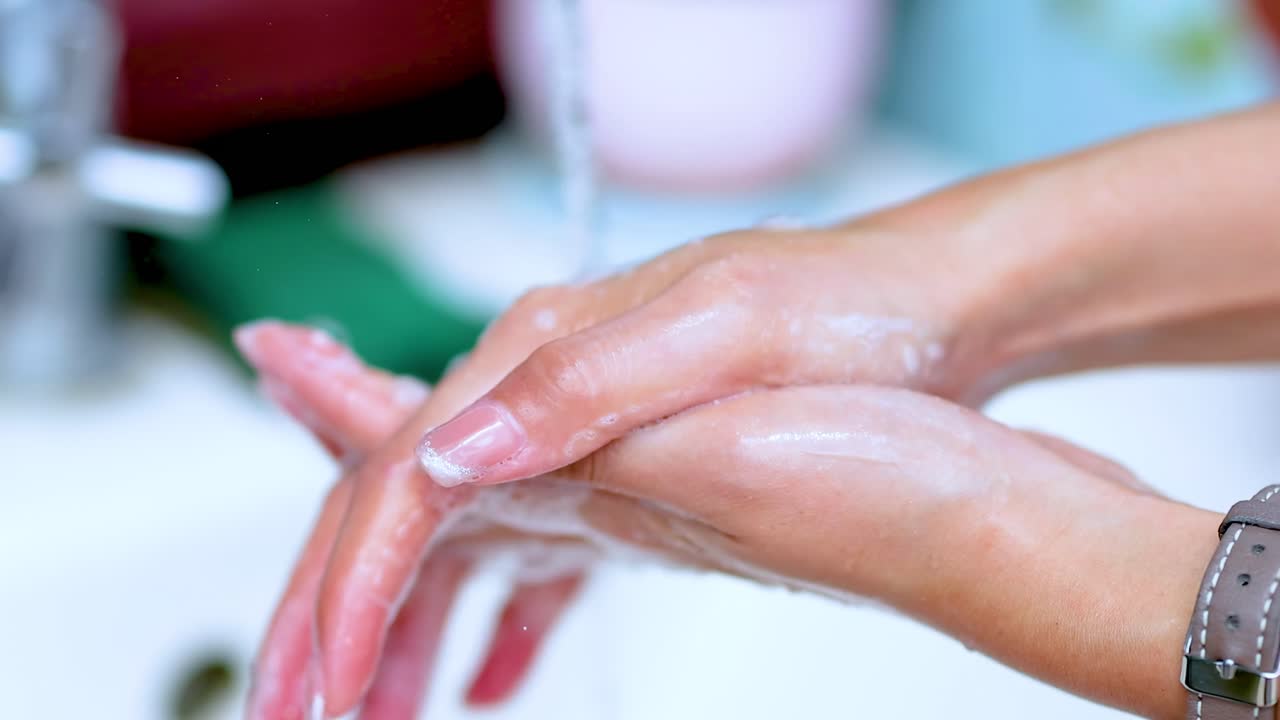 Detailed view of hands being washed with soap under running water, showcasing lather and cleanliness.