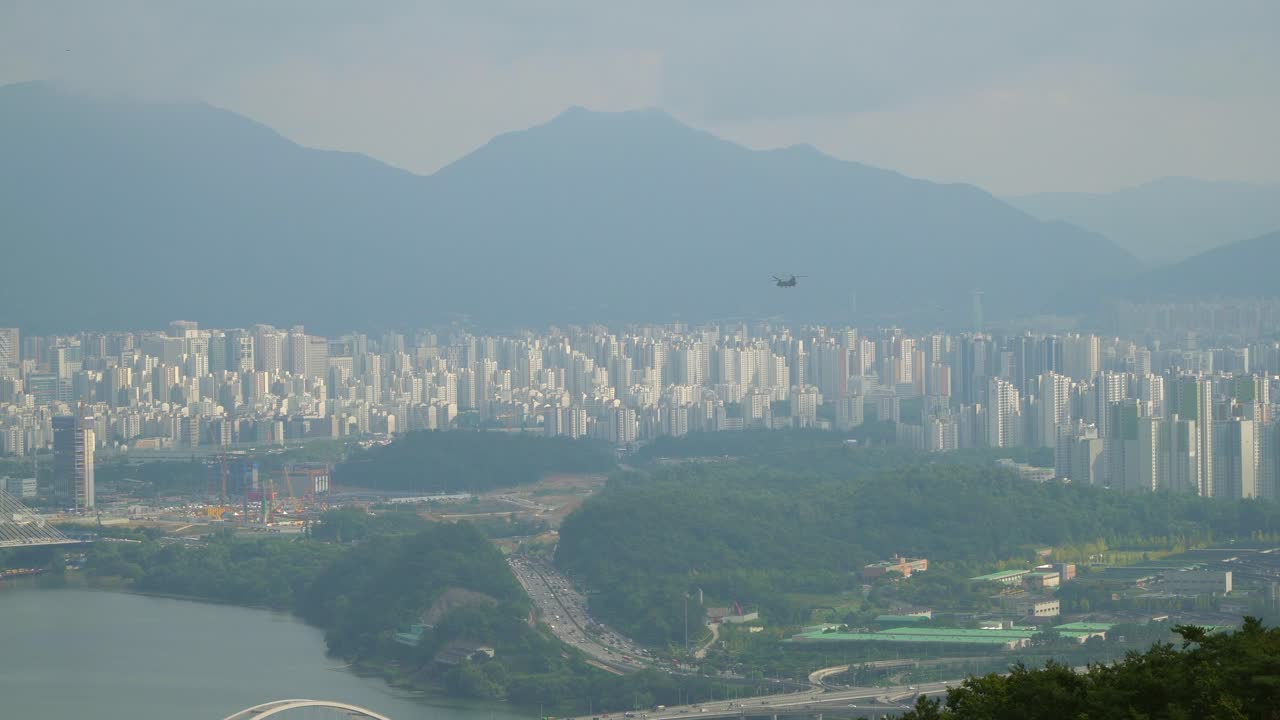 helicóptero de carga boeing ch-47 chinook sobrevolando seúl en el horizonte urbano de la ciudad y el fondo de las montañas en un día brumoso, vista desde la antena del pico de la montaña acha