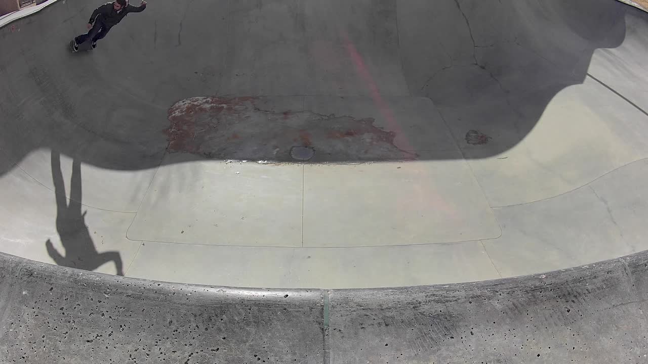 긴 머리 히스패닉 스케이트 보더 뒷면 조각 얼음 채워진 스케이트 풀, 높은 각도 와이드 샷