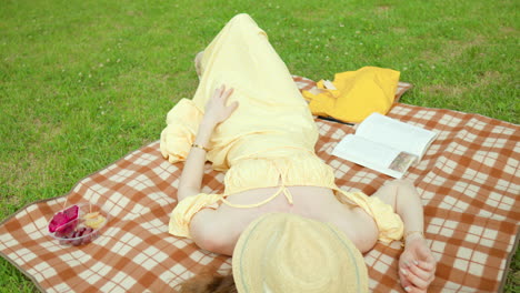 dolly out revealing a woman lying on a picnic blanket on lawn with a book beside her