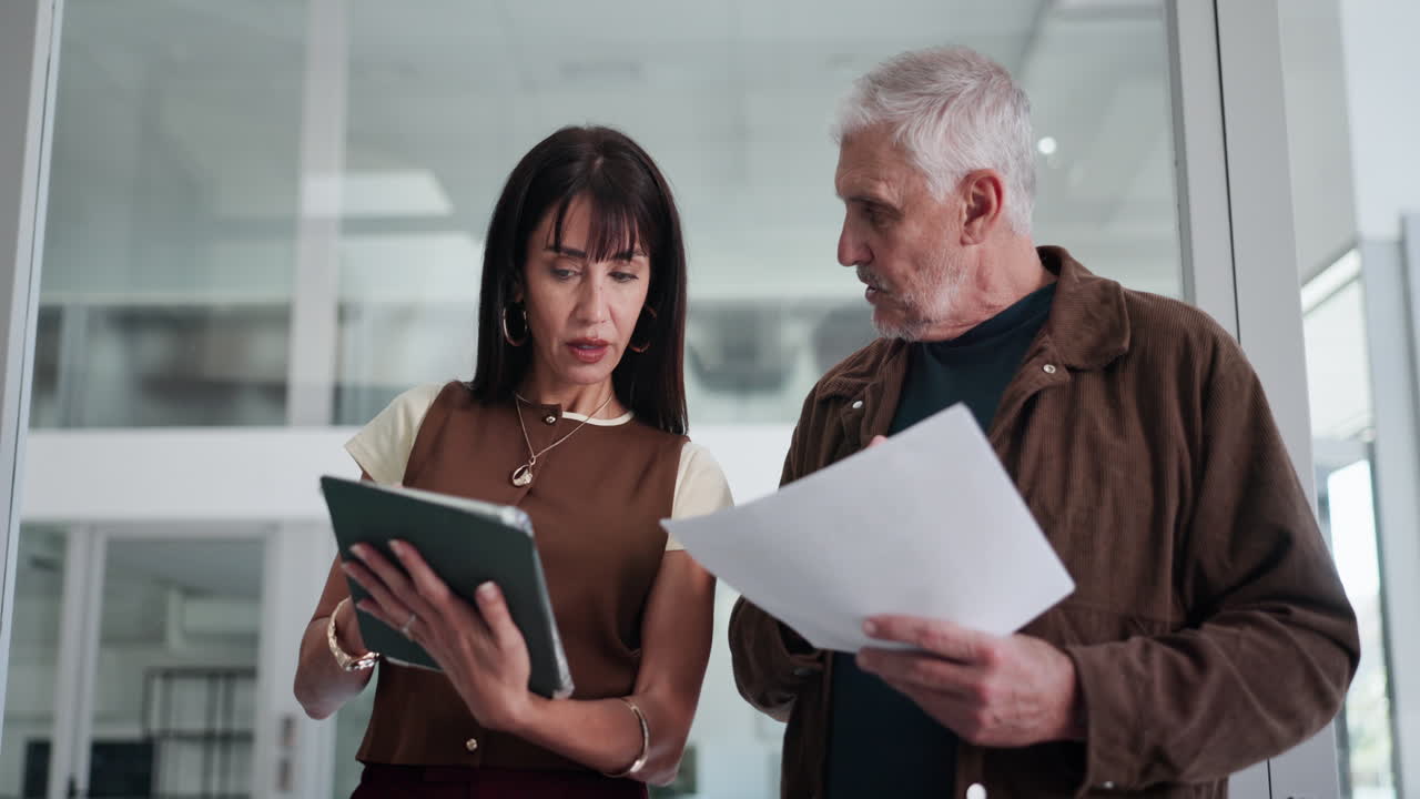 Two Business People Discussing Documents and Tablet in Modern Office