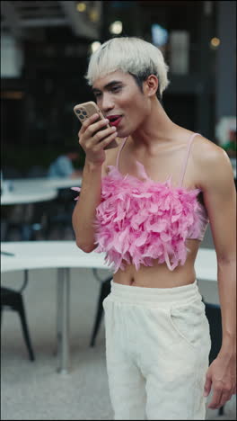 man using phone in a cafe wearing pink feathered top and white pants