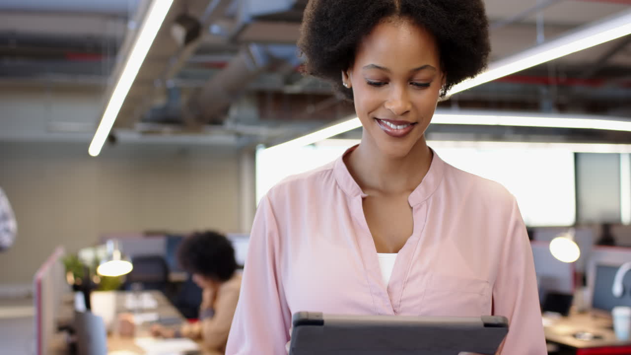 African American woman using tablet in modern office, open workspace with colleagues