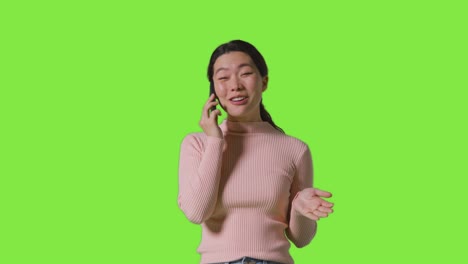 studio shot of smiling woman talking on mobile phone against green screen