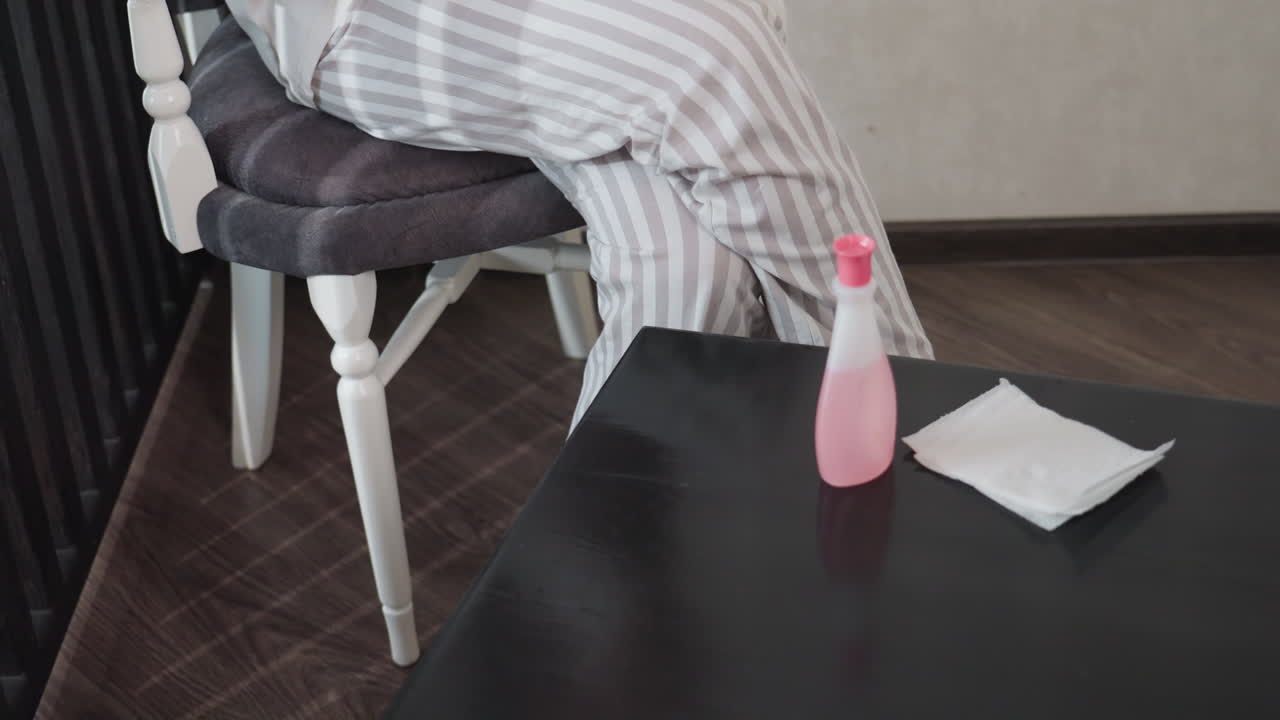 Elegant woman bends forward to place nail polish, remover, wiper on table before sitting on chair, long brunette hair with blonde highlights, soft indoor light, studio background, calm mood
