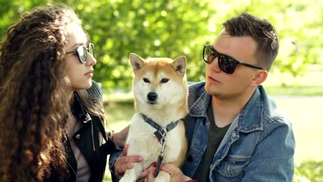 loving owners of beautiful dog shiba inu are kissing the animal and petting it on the head while resting in the park together. love, pets and healthy lifestyle concept.