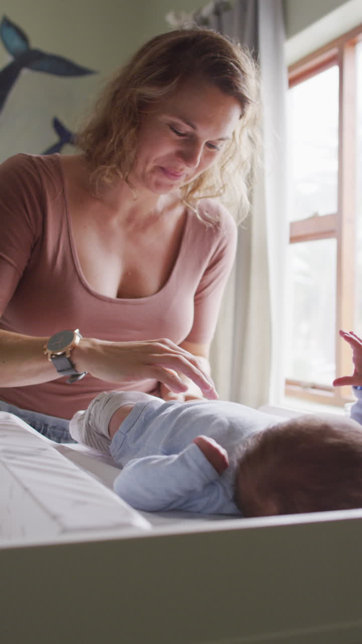 video vertical de una madre caucásica feliz cambiando a un bebé recién nacido