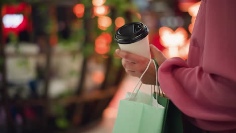 hand view of a lady in pink dress holding a coffee cup while walking in a restaurant, the background features blurred chairs, tables, glowing red lights, and people walking by around