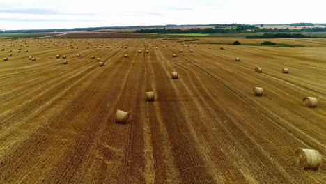 Aerial-flyover-yellow-field-after-harvest-with-hay-bales-in-countryside-during-sunny-day