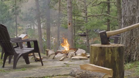 an axe is embedded in a log near an outdoor fire pit with a blazing fire