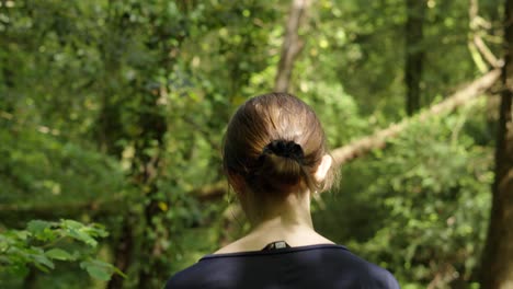 Mujer-Con-Gafas-De-Sol-Mirando-árboles-Altos-Caminando-En-El-Bosque-En-Un-Día-Soleado---Tiro-De-Seguimiento