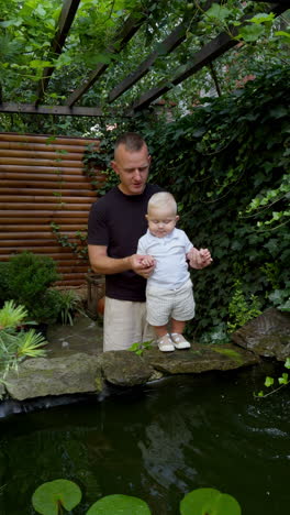 approaching father and son standing close to the fountain. daddy holds his baby looking at water. vertical video.