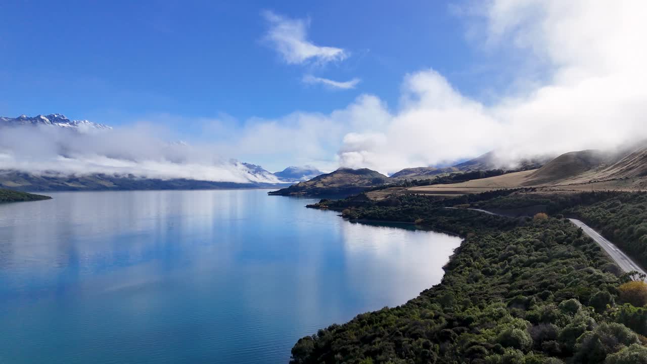 Drone captures stunning aerial views of Lake Wakatipu, winding roads, and lush greenery under clear blue skies in Glenorchy, New Zealand