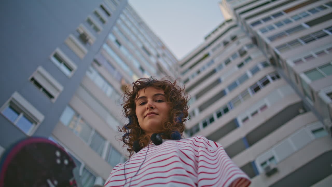 adolescente rizado sosteniendo una tabla de skate en la calle vista de abajo de cerca. mujer longboard