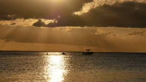 Ein-Sportboot,-Das-Einen-Großen-Wagen-Mit-Menschen-Darin-Zieht-Und-über-Das-Sonnenlicht-Fährt,-Das-Sich-Unter-Lichtstrahlen-Spiegelt,-Die-Durch-Die-Wolken-Fallen