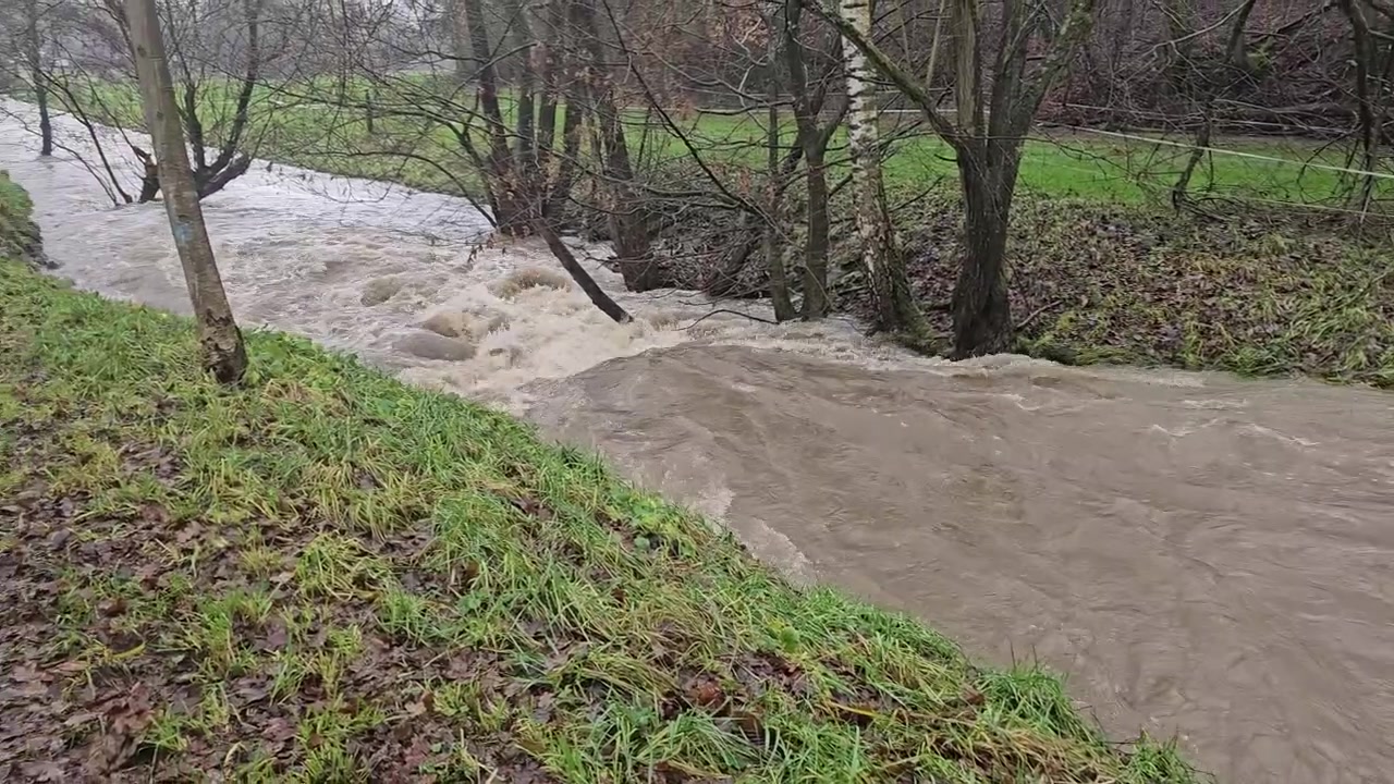 Turbulent brown water from a swollen river overflowing its grassy banks next to a wet rural path