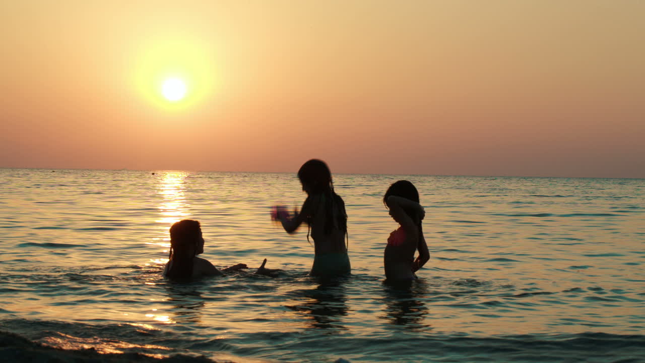 niñas jugando con la pelota en el mar al atardecer