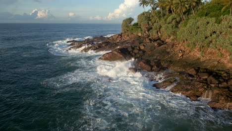 estableciendo una toma aérea de drones de pequeñas olas que se estrellan contra la costa rocosa en la costa sur tropical de sri lanka