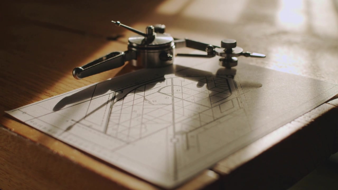 Opening frame drawing camera closer, highlighting metal compass on drafting board with plan