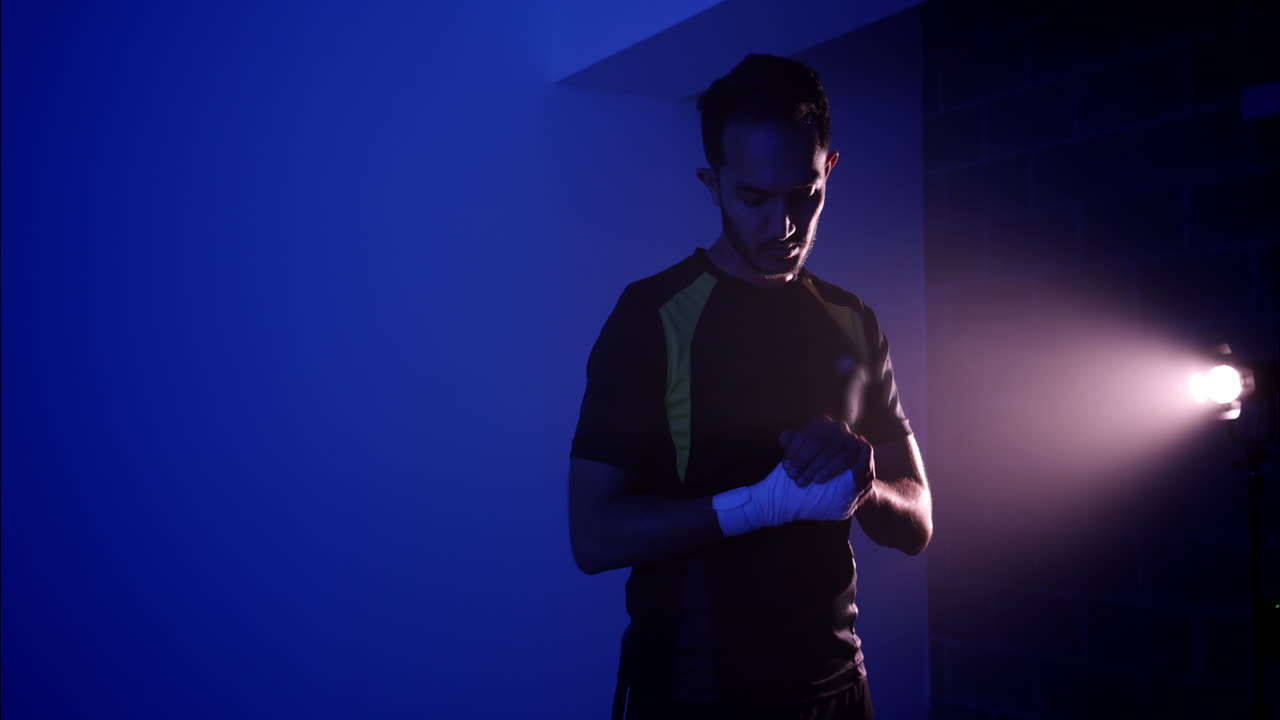 Pugile uomo che si fascia le mani con fasce da boxe bianche in una palestra buia