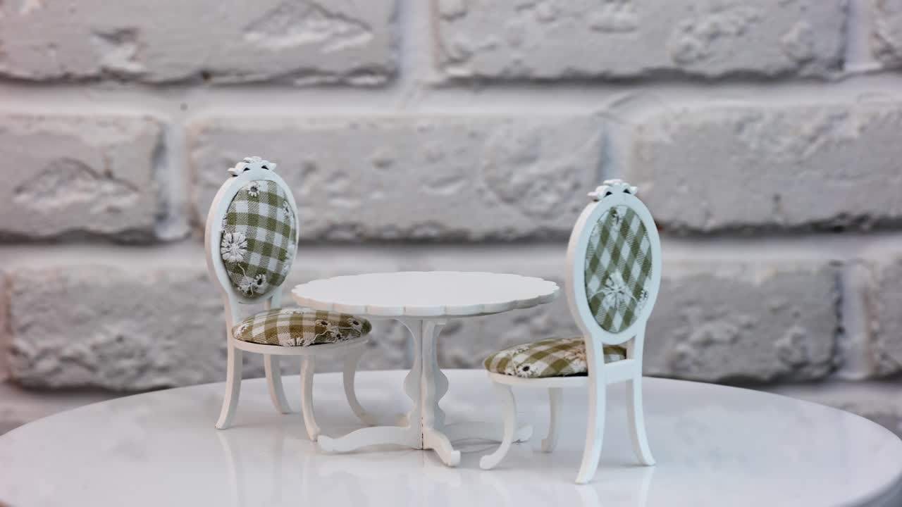 Toy furniture set containing a table and two chairs. White one-leg table and chairs with colored casing on the rotating stand. Close up.