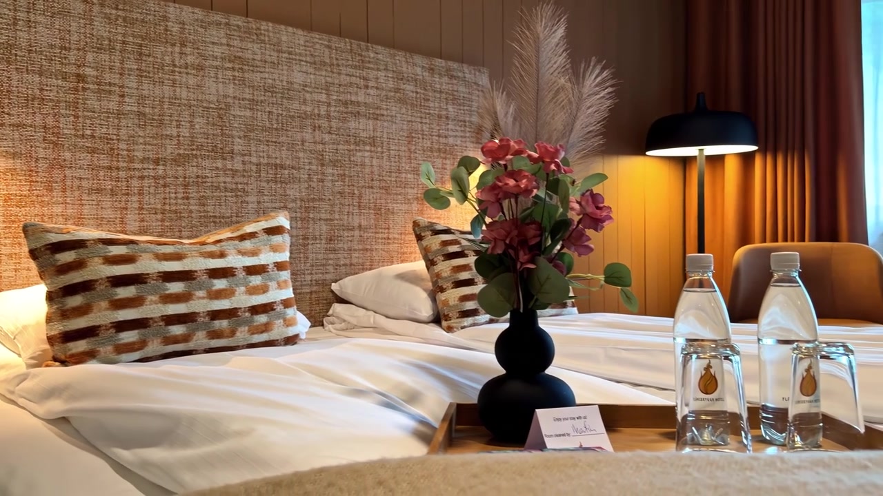 Koselig hotellrom med enkeltsenger, pynteputer, blomster og flaskevann