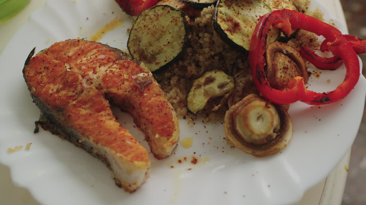 Close-up of a grilled salmon steak served with quinoa and roasted vegetables on a white plate, shot in natural light