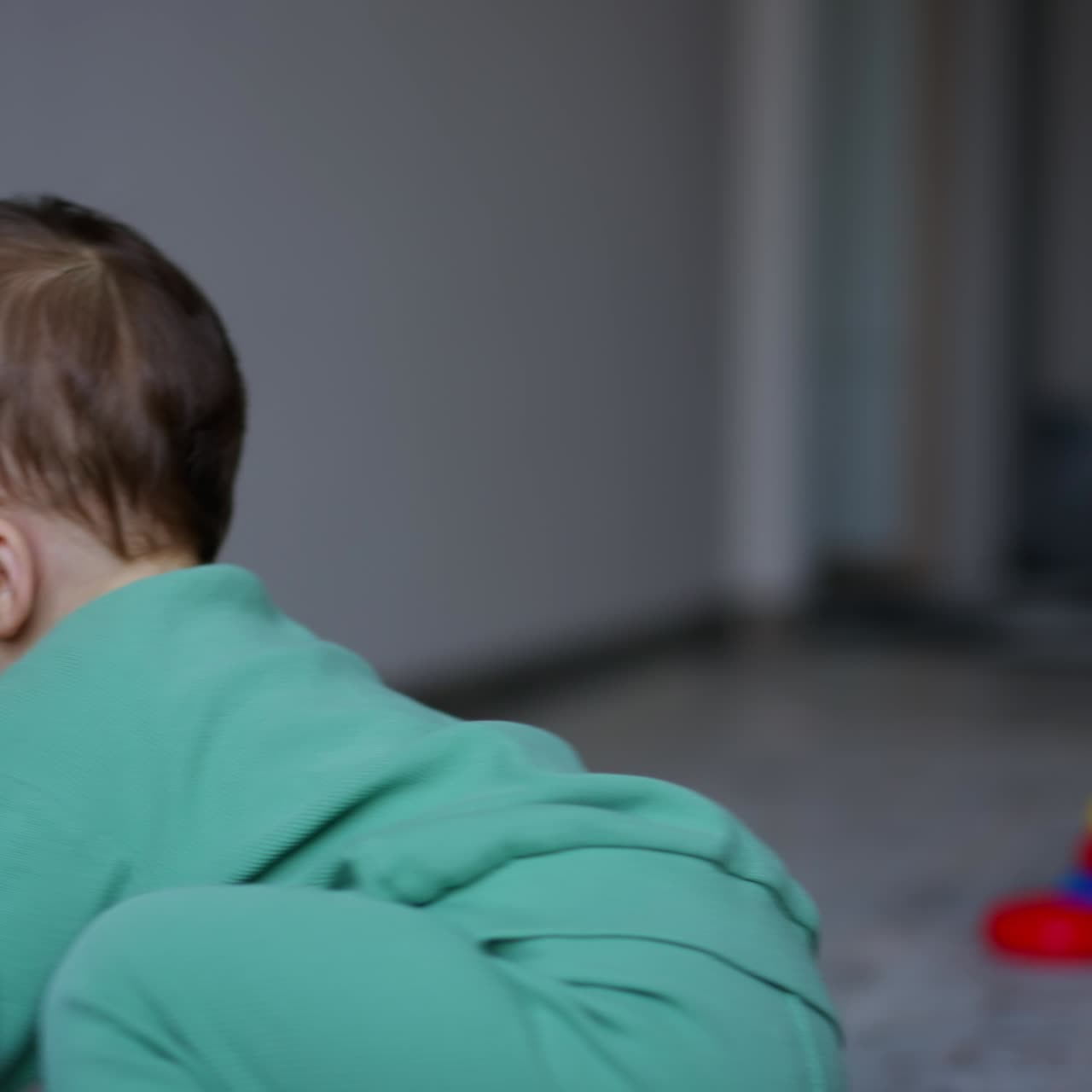 Un neonato seduto in casa guarda l'anello giocattolo rotolare sul pavimento. Vista laterale. Il bambino prende il giocattolo e lo lancia.