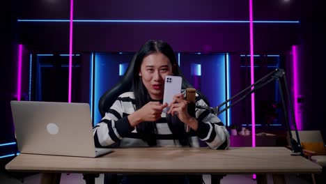 a smiling asian woman with computer reviewing phone in room lit by neon lights in retro
