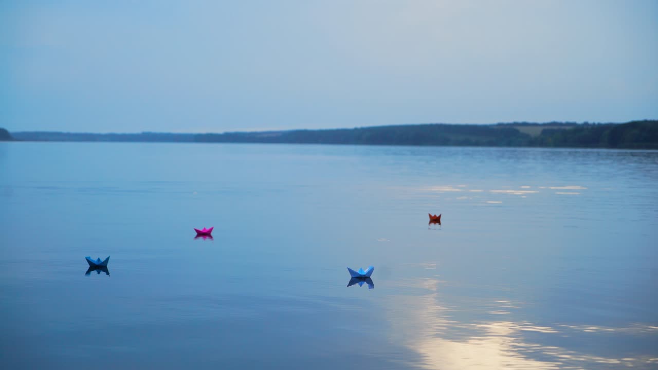 Beautiful evening scenery of a calm river and colored paper boats on water background. Four origami ships floating at sunset