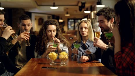 cheerful young people are eating, drinking, chatting and laughing at table in modern cafe. mates are wearing casual clothes. snacks and glasses in foreground.