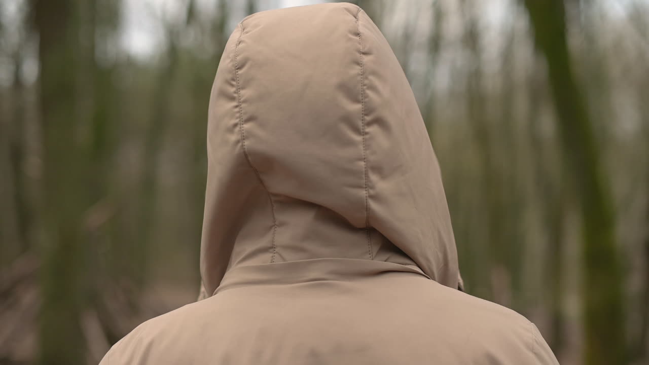 한 어린 소녀가 숲을 걷고 코트의 후드를 벗습니다.