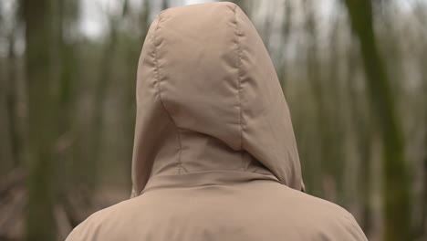 a young girl walks through the forest and removes the hood of her coat