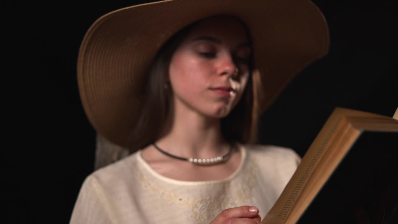 Una donna adulta parzialmente visibile tiene un libro rilegato aperto su uno sfondo scuro, con una luce calda e soffusa che evidenzia il suo viso, la mano e le spalle