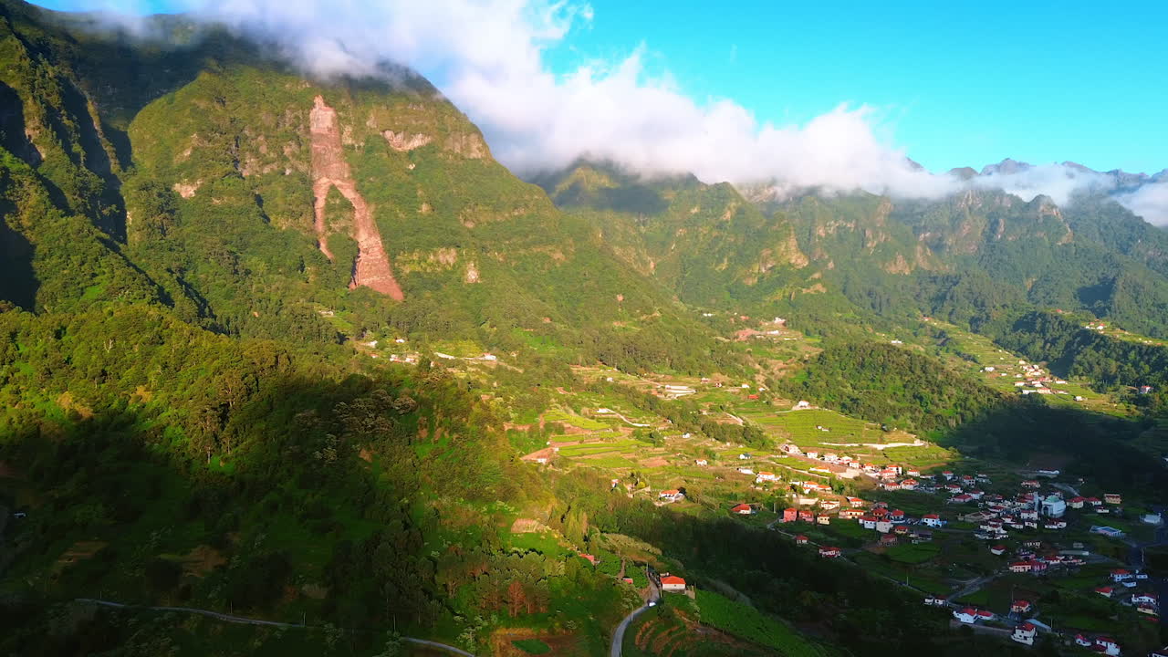 Beautiful picturesque town locating in the surrounding of stunning mountains. Fluffy white cloudscape hanging above the rocks. Madeira, Portugal.